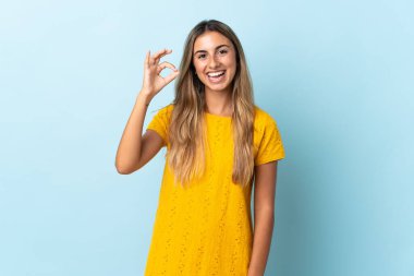 İzole edilmiş mavi arka planda genç İspanyol kadın parmaklarıyla işaret veriyor.