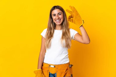 Genç İspanyol elektrikçi kadın izole edilmiş sarı duvarın üzerinde parmaklarıyla işaret gösteriyor.