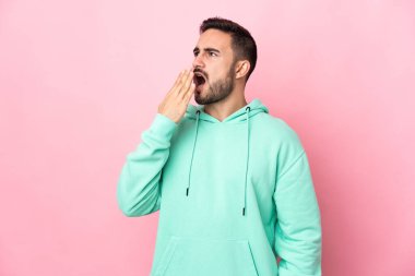 Young caucasian handsome man isolated on pink background yawning and covering wide open mouth with hand