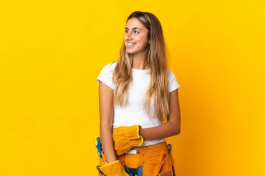 Genç İspanyol elektrikçi kadın izole edilmiş sarı duvarın üzerinden yan tarafa bakıyor ve gülümsüyor.