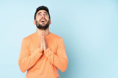 Beyaz tenli yakışıklı adam avucunu bir arada tutuyor. Kişi, izole edilmiş mavi bir arkaplan istiyor.