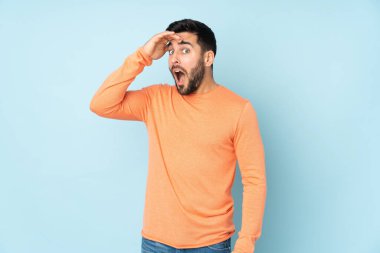 Kafkasyalı yakışıklı adam, yalıtılmış mavi arka plana bakarken sürpriz bir hareket yapıyor.