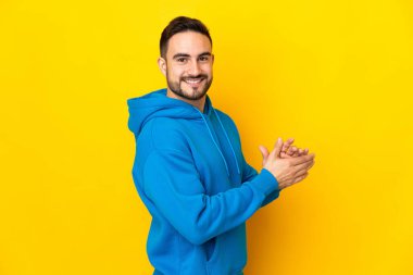 Sarı arka planda izole edilmiş beyaz, yakışıklı bir adam alkışlıyor.