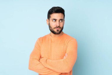 Kollarını kapalı tutan beyaz, yakışıklı bir adam izole edilmiş mavi arka plan