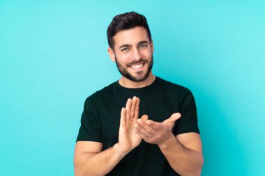 Beyaz tenli yakışıklı adam mavi arka planda izole edilmiş bir konferansta sunumdan sonra alkışlıyor.