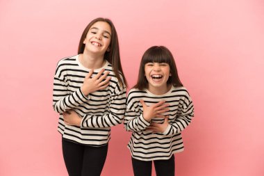 Küçük kız kardeşler pembe arka planda izole edilmiş, gülümseyen ve ellerini göğsüne koyan kızlar.