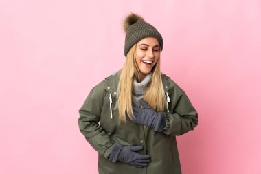 Pembe arka planda izole edilmiş, kış şapkalı genç bir kadın. Çok gülümsüyor.
