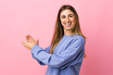 Soyutlanmış pembe arka planı alkışlayan genç bir kadın.