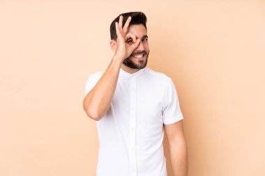 Beyaz tenli yakışıklı adam bej arka planda izole edilmiş. Parmaklarıyla tamam işareti gösteriyor.