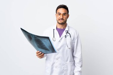 Beyaz arka planda izole edilmiş bir radyografi tutan genç bir doktor şüpheleri ve kafa karıştırıcı bir yüz ifadesi var.