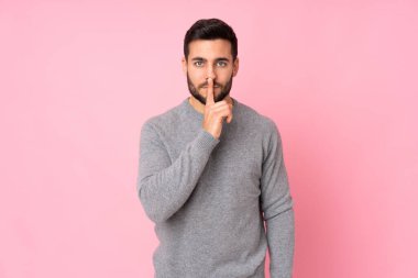 Kafkasyalı yakışıklı adam izole edilmiş arka planda sessizlik işareti gösteriyor. Parmağını ağzına sokuyor.