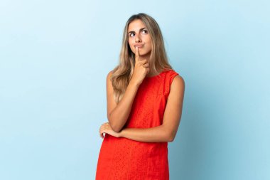 İzole edilmiş mavi arka planda genç bir İspanyol kadının yukarı bakarken şüpheleri var.