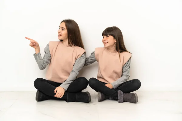 Irmãzinhas Sentadas Chão Isoladas Fundo Branco Apontando Para Lado Para — Fotografia de Stock