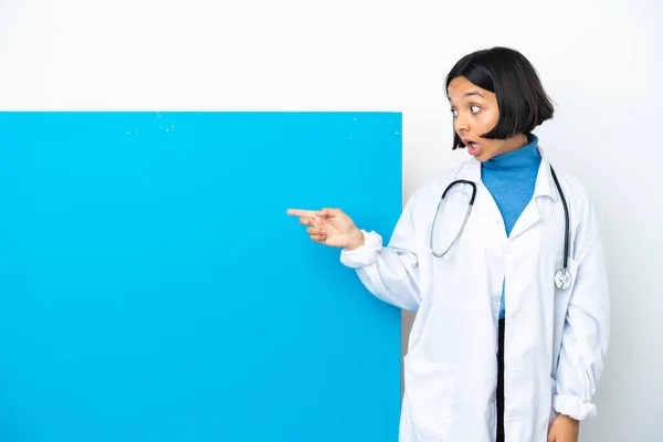 年轻的混合种族医生女人 有一个白色背景的大标语牌 带着惊讶的表情 同时指向一边 — 图库照片