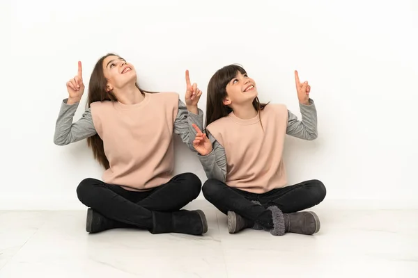 Irmãzinhas Sentadas Chão Isoladas Fundo Branco Apontando Com Dedo Indicador — Fotografia de Stock