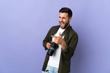 İzole edilmiş mor arkaplan üzerinde fotoğrafçı parmak göstererek bir ürün sunar.