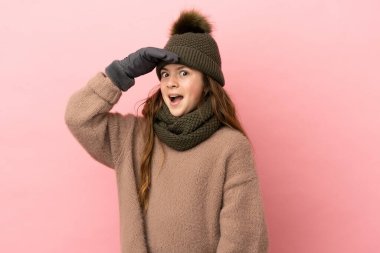 Pembe arka planda izole edilmiş küçük bir kız. Yan tarafa bakarken sürpriz jest yapıyor.