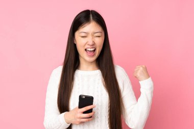 Asyalı genç bir kadın izole edilmiş arka planda, telefon zafer pozisyonunda.