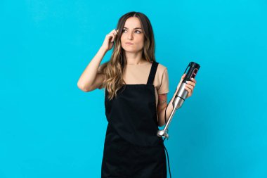 Mavi arka planda izole edilmiş el blenderi kullanan Romen kadının şüpheleri ve düşünceleri var