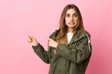 Soyutlanmış pembe arka planı olan genç bir kadın korkmuş ve kenarı işaret ediyor.