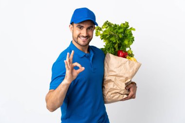 Beyaz arka planda izole edilmiş sebzeli teslimatçı tamam işareti parmaklarıyla gösteriyor.