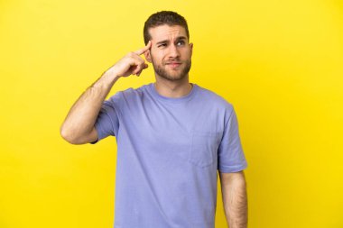 Sarışın, soyutlanmış, sarı arka planda yakışıklı bir adam. Delilik jesti yapıyor. Parmağını başına koyuyor.