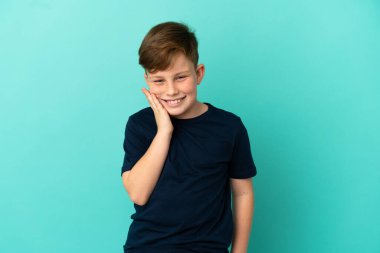 Küçük kızıl saçlı çocuk mavi arka planda diş ağrısı ile izole edilmiş.