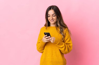 Pembe arka planda izole edilmiş genç Romen kadın cep telefonuyla mesaj gönderiyor