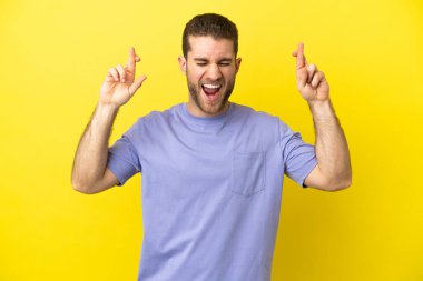 Sarışın yakışıklı, izole edilmiş sarı arka planda, parmakları çapraz