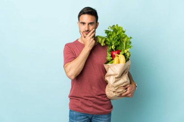 Kafkasyalı genç bir adam mavi arka planda izole edilmiş sebze alıyor.