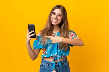 İzole edilmiş sarı arka plan üzerinde cep telefonu kullanan genç bir kadın.