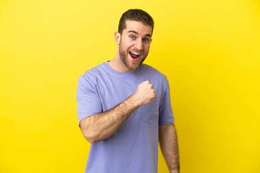 Sarışın yakışıklı adam izole edilmiş sarı arka planda zaferi kutluyor.