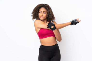 Genç Afrikalı Amerikalı spor kadın beyaz arka planda izole edilmiş kollarını esnetiyor.
