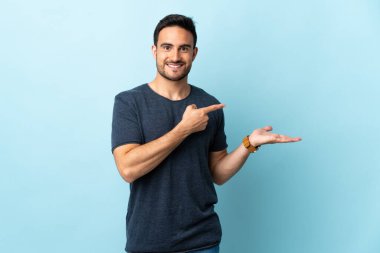 İzole edilmiş arka planda genç yakışıklı bir adam. Avucunun içine reklam koymak için hayali bir alan tutuyor.