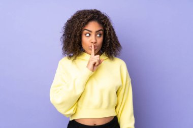 Genç Afrikalı Amerikalı bir kadın arka planda izole edilmiş. Sessiz bir jest işareti var. Parmağını ağzına sok.