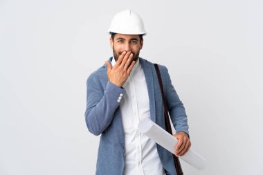 Miğferli ve elinde planları olan genç bir mimar beyaz arka planda izole edilmiş mutlu ve gülümseyen ağızlarını eliyle kapatıyor.