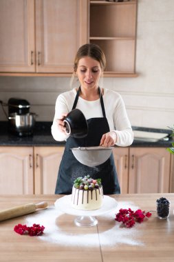Genç pasta şefi lezzetli ev yapımı beyaz çikolatalı kek pişiriyor ve mutfakta meyveler var.