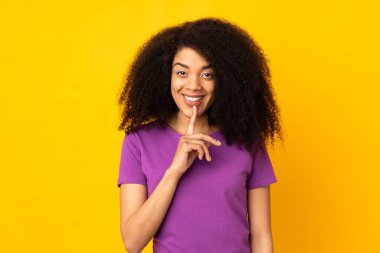 Genç Afrikalı Amerikalı kadın izole edilmiş geçmişinde parmağını ağzına sokan sessiz bir jest işareti gösteriyor.