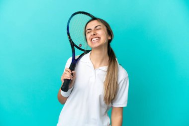 Genç bayan tenisçi mavi arka planda tek başına gülüyor.