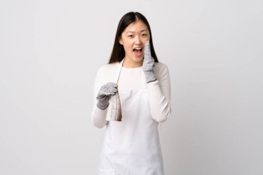 Çinli balıkçı önlük takıyor ve çiğ balığı izole edilmiş beyaz arka planda tutup ağzı açık bağırıyor.