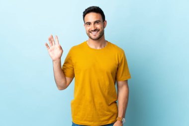 Genç yakışıklı adam, izole edilmiş arka planda mutlu bir ifadeyle selamlıyor.