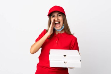 Pizza teslimatçısı kadın elinde pizza tutuyordu. Koronavirüsten koruyordu. İzole edilmiş beyaz bir duvarın üzerinde ağzı açık bir şekilde bağırıyordu.