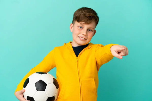 Malý Ryšavý Chlapec Izolované Modrém Pozadí Fotbalovým Míčem Ukazuje Dopředu — Stock fotografie