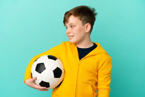 Redhead Παιδί Παίζει Ποδόσφαιρο Απομονώνονται Μπλε Φόντο Αναζητούν Πλευρά — Φωτογραφία Αρχείου