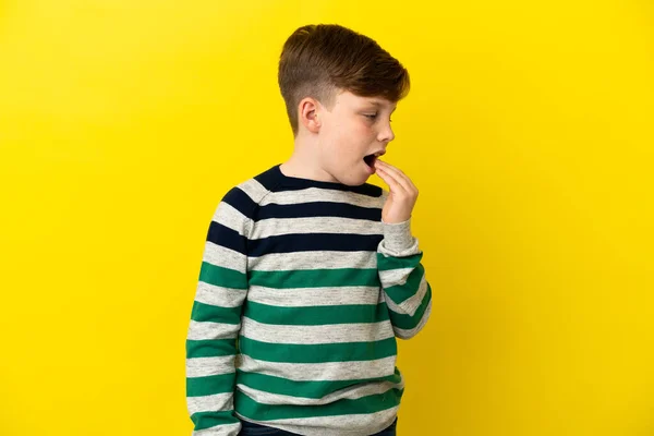 小さな赤い頭の男の子孤立した上黄色の背景Yawningとカバー広いオープン口で手 — ストック写真