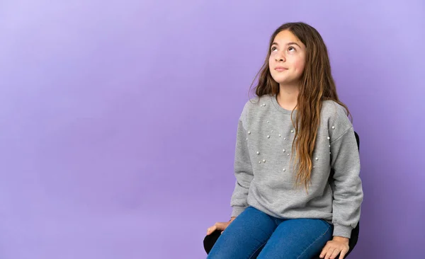 Menina Caucasiana Sentada Uma Cadeira Isolada Fundo Roxo Olhando Para — Fotografia de Stock