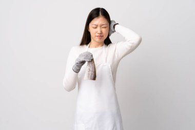 Çinli balıkçı önlük takıyor ve çiğ balığı izole edilmiş beyaz arka planda tutuyor. Hayal kırıklığına uğramış ve kulakları tıkamış.