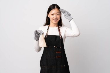 Çinli balıkçı önlük takıyor ve çiğ bir balığı izole edilmiş beyaz arka planda tutuyor mutlu bir ifadeyle selamlıyor.