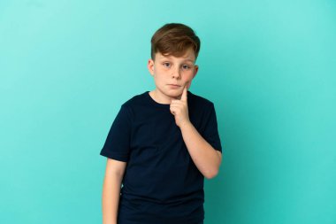 Küçük kızıl saçlı çocuk mavi arka planda izole edilmiş ve düşünüyor