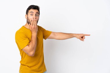 Beyaz arka planda sakallı yakışıklı genç bir adam. Sürpriz bir ifadeyle işaret ederken...